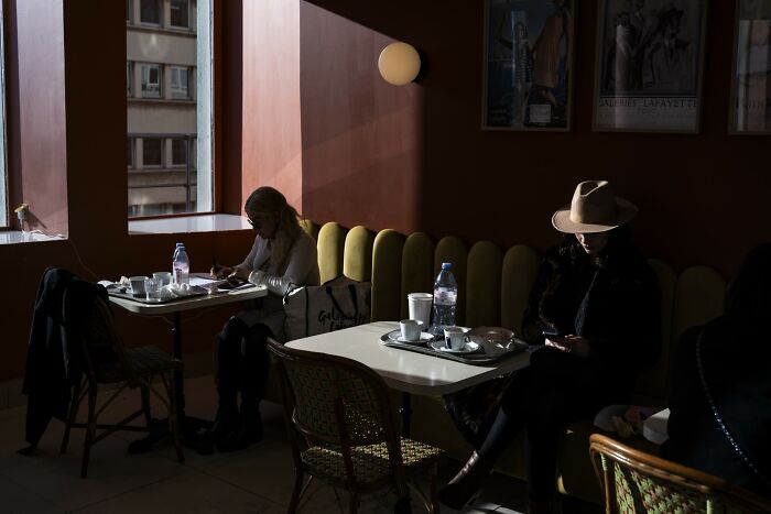 A woman in a cafe with a hat, a Macadam Awards street photo of life's funniest coincidences.