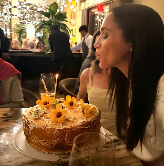 Meghan Markle blowing out candles on a birthday cake with yellow flowers, receiving Karma on her birthday. Meghan Markle blowing out candles on a birthday cake with yellow flowers, receiving Karma on her birthday.