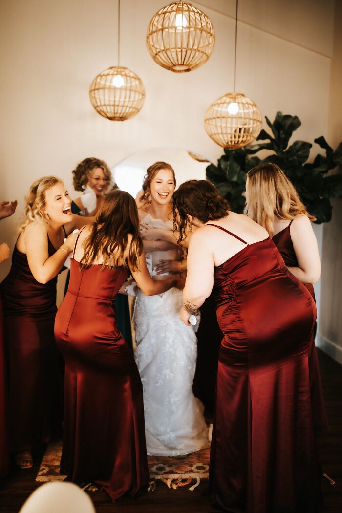 Bridesmaids laughing while helping a bride get ready, capturing funny wedding moments.