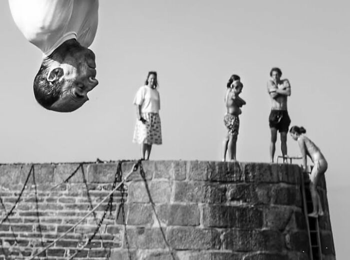 A man performing a backflip over a wall, with onlookers below, in a perfectly timed street photo of Paris.