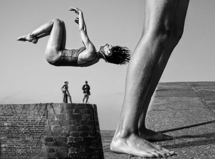 A woman leaps into the air beside giant legs, a perfectly timed street photo in Paris.