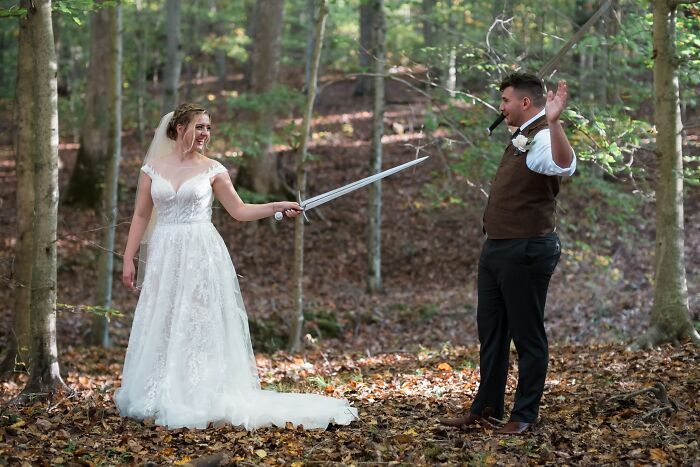 Bride holding a sword playfully at the groom in a forest, captured in an iconic funny wedding photo.