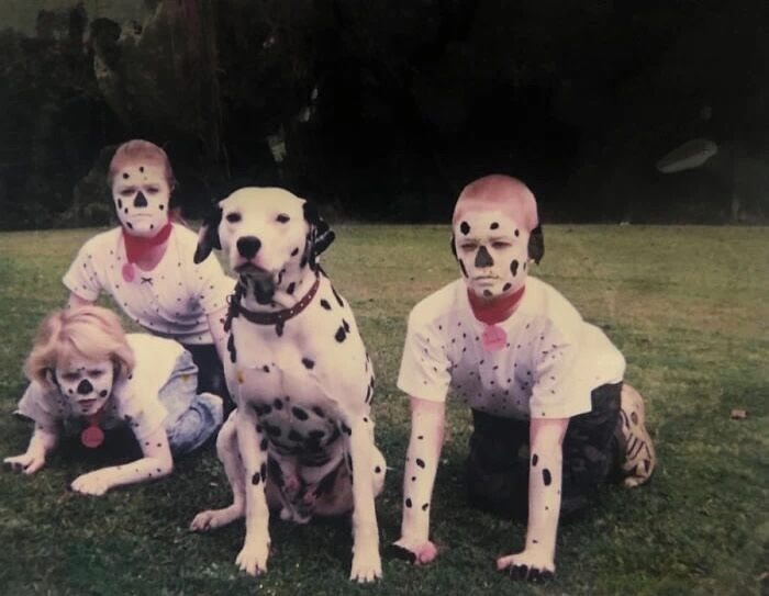 An absurd dog image of a Dalmatian dog sitting in grass with three children in dalmatian costumes.