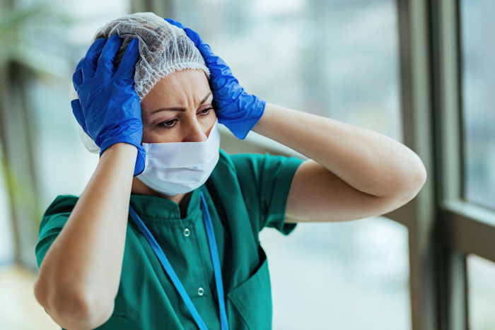 A stressed ER nurse wearing a mask and scrubs, holding her head, reflecting the intensity of saving a patient. A stressed ER nurse wearing a mask and scrubs, holding her head, reflecting the intensity of saving a patient.