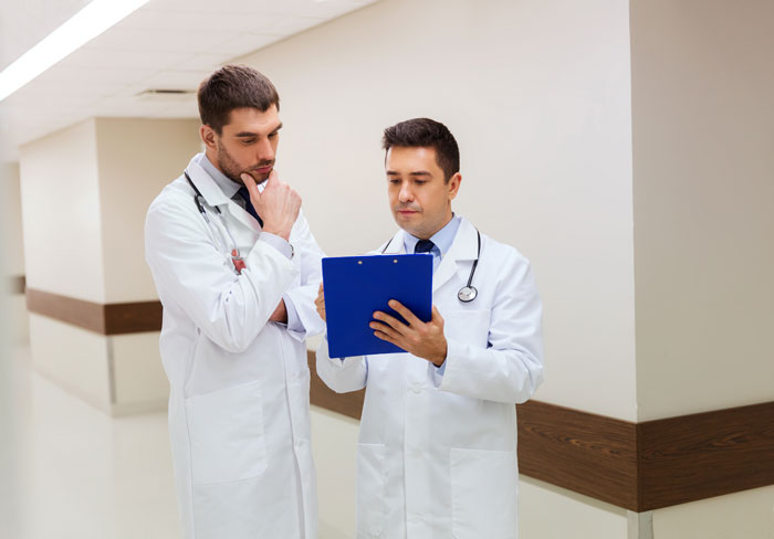 Two doctors in white coats review a chart, discussing a patient's condition after routine surgery and amputation. Two doctors in white coats review a chart, discussing a patient's condition after routine surgery and amputation.