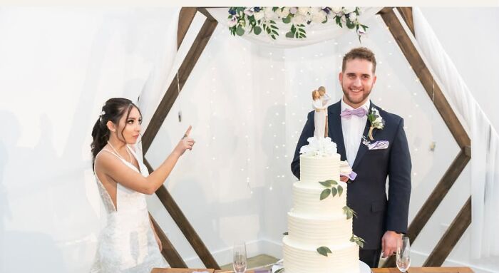 Bride pointing at groom next to a tall wedding cake, creating a funny wedding photo.