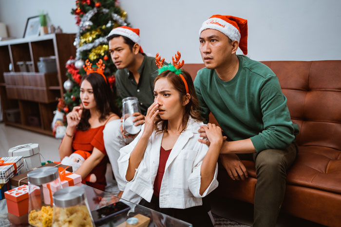 People watching a screen with worried expressions, one woman pinching her nose, on Christmas. They fired workers.