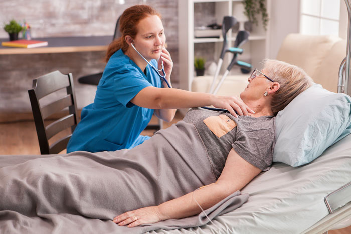 An ER nurse checks an elderly patient's heartbeat with a stethoscope in a hospital room. An ER nurse checks an elderly patient's heartbeat with a stethoscope in a hospital room.