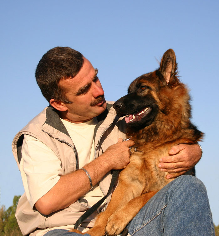 A man lovingly embraces his senior dog, a German Shepherd, against a clear blue sky, showing a strong bond. A man lovingly embraces his senior dog, a German Shepherd, against a clear blue sky, showing a strong bond.