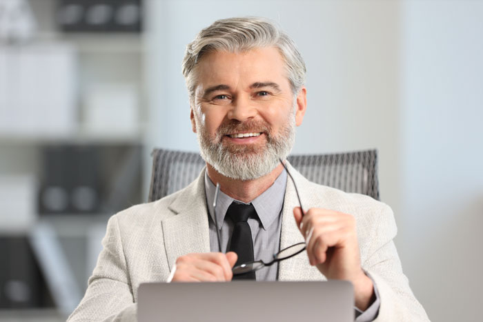 A smiling, professional man with gray hair and a beard, wearing a suit, holding glasses, symbolizing a positive outcome for the ER nurse. A smiling, professional man with gray hair and a beard, wearing a suit, holding glasses, symbolizing a positive outcome for the ER nurse.