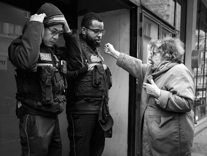 An elderly woman gesticulates at two police officers, a perfectly timed street photo in Paris.