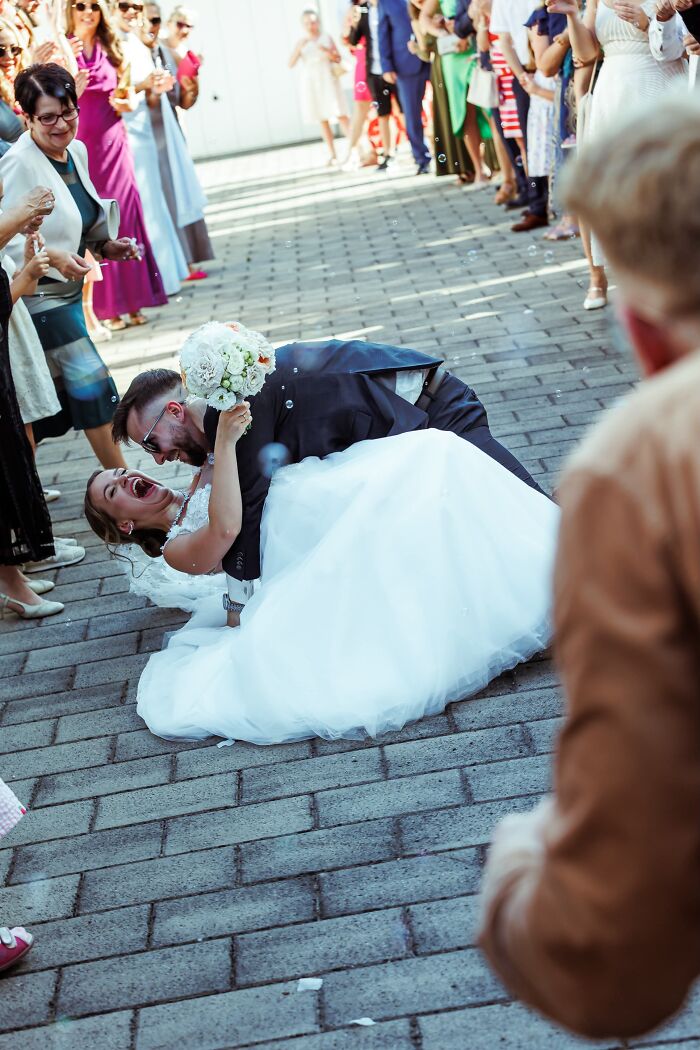 A groom dips his laughing bride low, almost to the ground, a funny wedding photo capturing an iconic, joyful moment.
