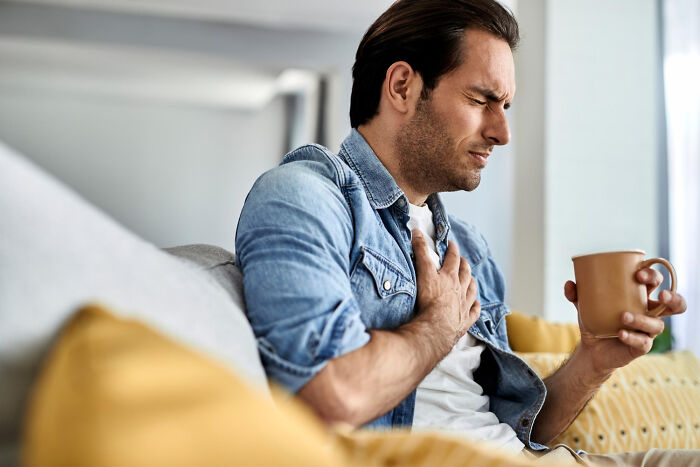 A man clutches his chest in pain while holding a mug, representing incredible stories about life and what comes after.