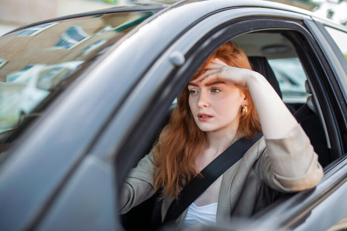 A woman with red hair looking stressed in a car, contemplating her therapy experiences and why she left.