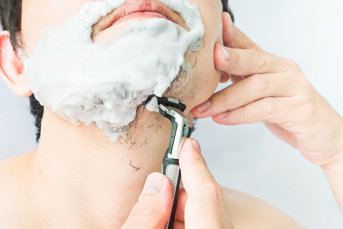A man shaving his beard with shaving cream and a razor, demonstrating a common personal grooming poverty habit.