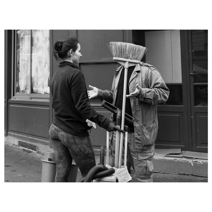 A woman talks to a street performer with a broom for a head in a perfectly timed street photo in Paris.