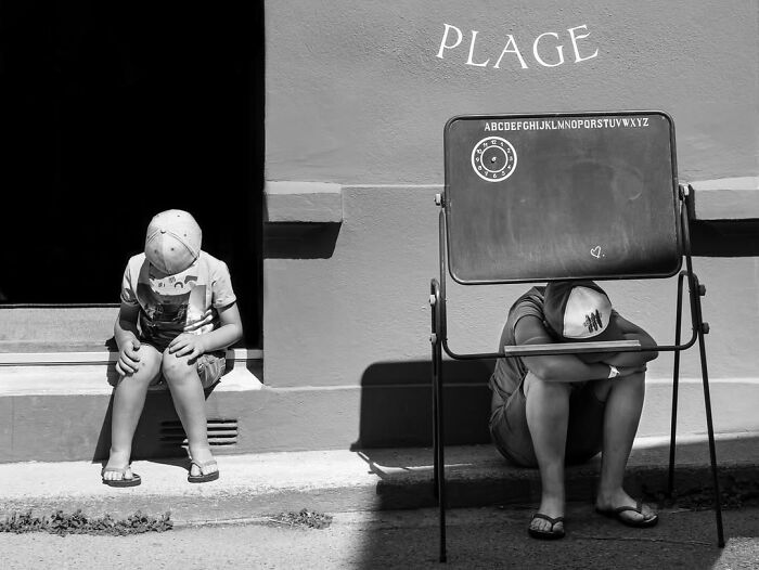 Two boys sitting on steps by a chalkboard with Plage written above, a perfectly timed street photo in Paris.