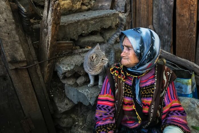 Murat Bakmaz captures the beauty of everyday life: An elderly woman in a headscarf next to a cat on stone steps.