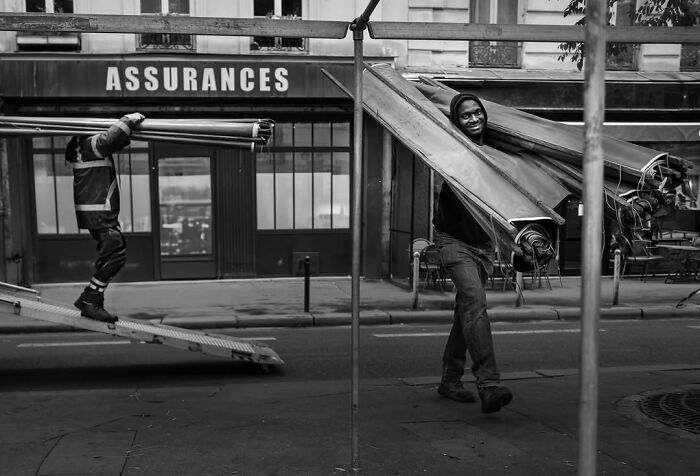 Two men carrying large awnings in front of an Assurances building in Paris, a perfectly timed street photo.