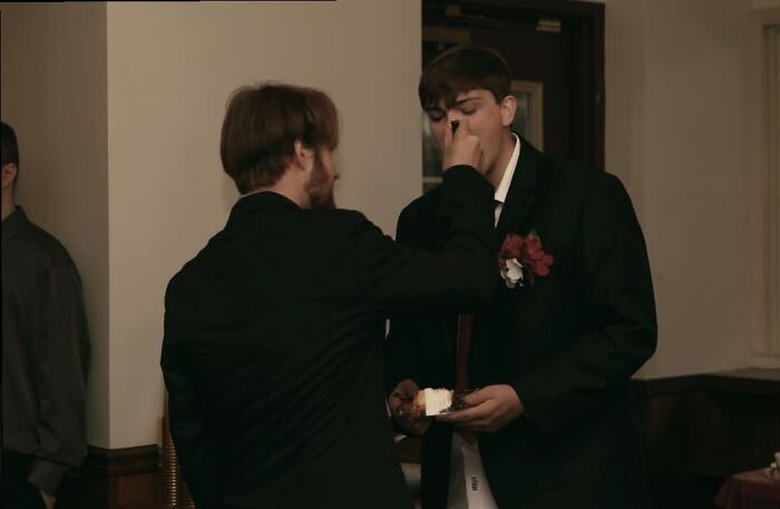 A funny wedding photo of one man playfully smearing cake on another man's nose, an iconic wedding moment.