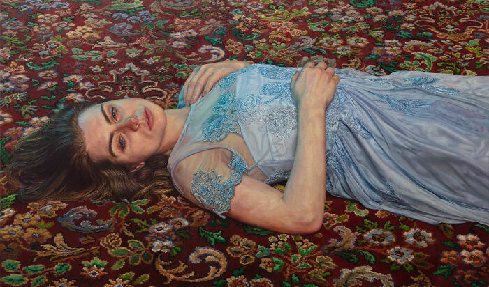 A hyperrealist painting by Ian Cumberland of a woman in a blue dress lying on a patterned rug with hidden meaning.