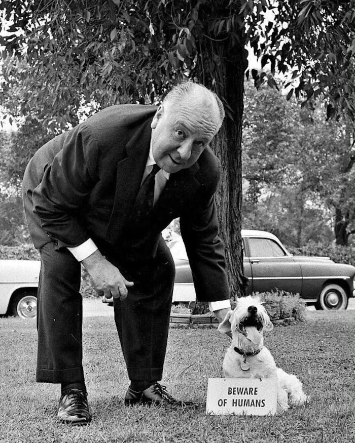 Artistic pure photography of Alfred Hitchcock with a dog and a 'Beware of Humans' sign.