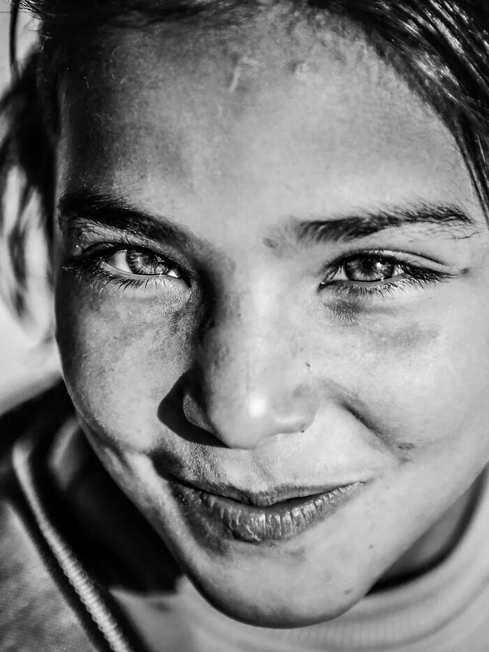 Perfectly timed street photo by Mehmet Bayram, a close-up of a smiling person's face with bright eyes.