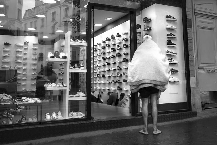 A person with a blanket over their head stands in front of a shoe store, a perfectly timed street photo in Paris.