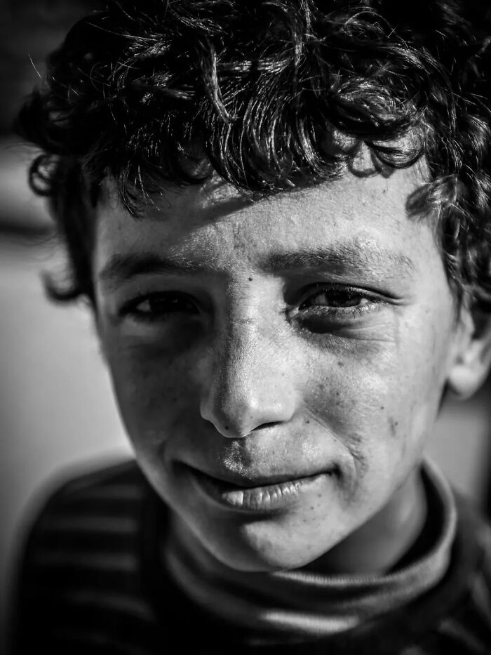 Perfectly timed street photo by Mehmet Bayram of a young person with curly hair, looking directly into the camera with a subtle smile.
