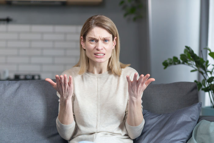 A woman with a confused and frustrated expression, hands open, sitting on a couch, deciding against family expectations to house her niece. A woman with a confused and frustrated expression, hands open, sitting on a couch, deciding against family expectations to house her niece.