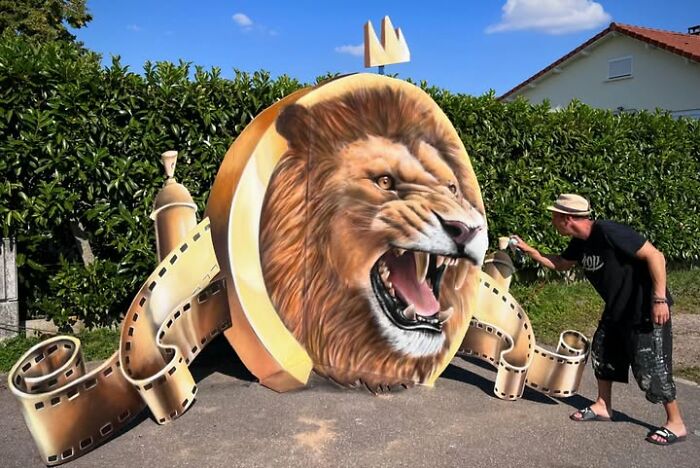 French artist painting a mind-bending 3D illusion of a roaring lion's head with film reel elements.