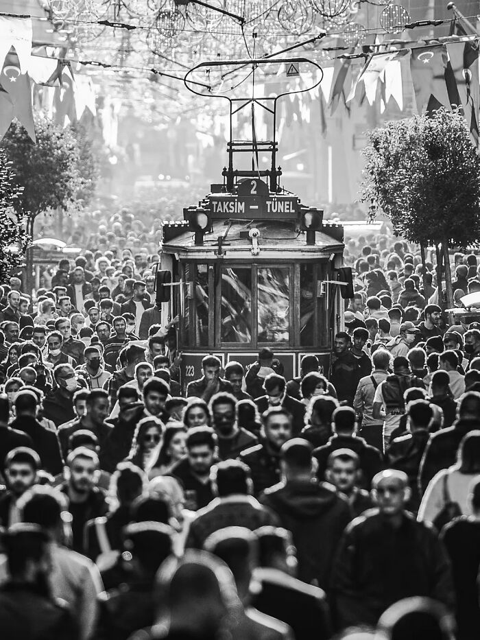Perfectly timed street photo by Mehmet Bayram with a crowded street, a tram in the background, and festive flags.