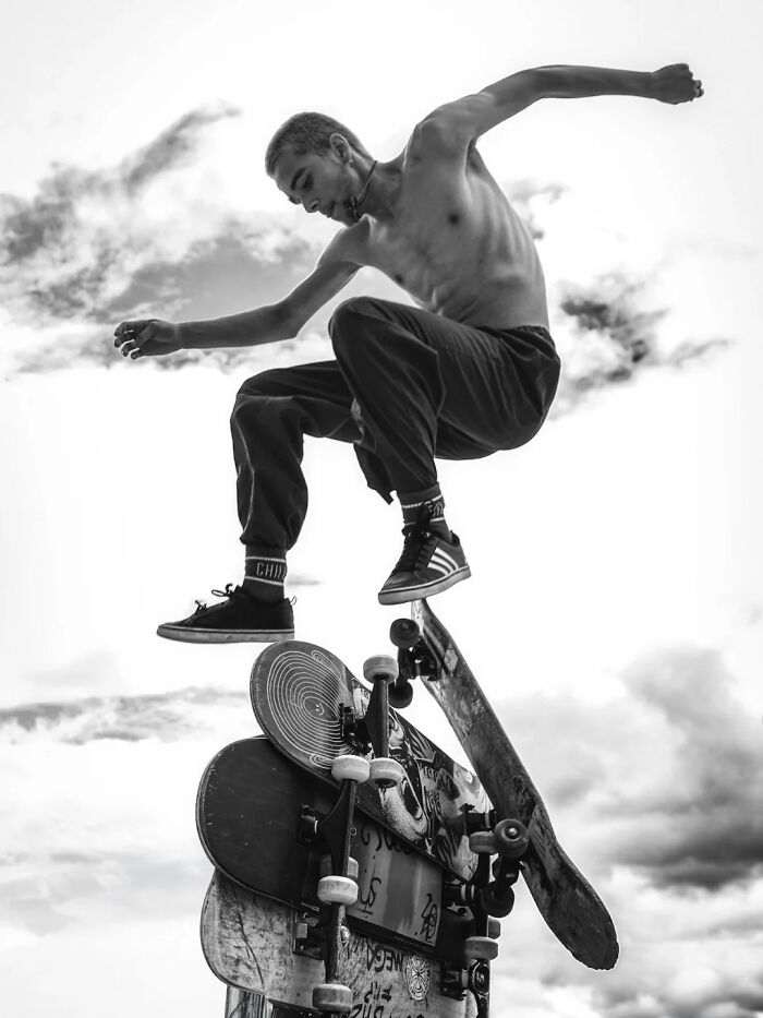 Perfectly timed street photo by Mehmet Bayram capturing a person balancing on stacked skateboards under a cloudy sky.