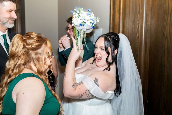Funny wedding photo of a bride joyfully making a rock-and-roll gesture while holding her bouquet.