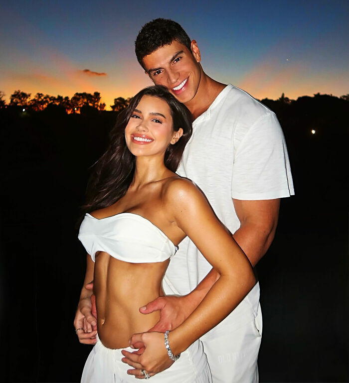 Pregnant influencer and the billionaire baby's dad posing together at sunset, both smiling brightly.