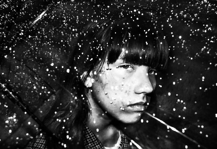 A black and white street photo of a young person's profile, illuminated by many small, bright dots, capturing the curiosity of childhood.