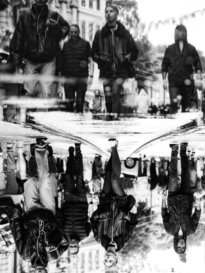 Perfectly timed street photo by Mehmet Bayram showing an upside-down reflection of people walking on a wet street.
