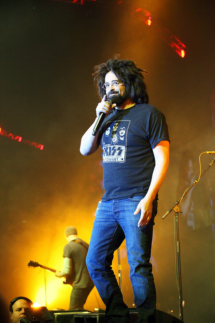 Adam Duritz performing live, showcasing his bio and career highlights, with his signature dreadlocks and glasses.