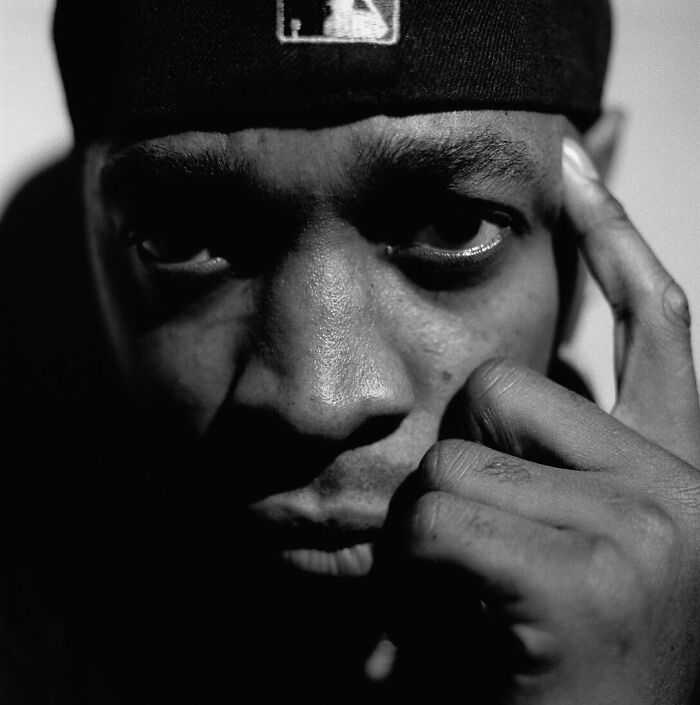 A black and white close-up of Chuck D looking intently at the camera, hand near his face. Highlights his career.