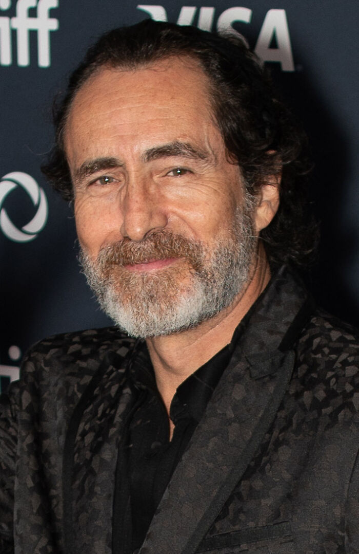 Demián Bichir smiles, showcasing his gray beard and dark patterned jacket, highlighting his bio and career.