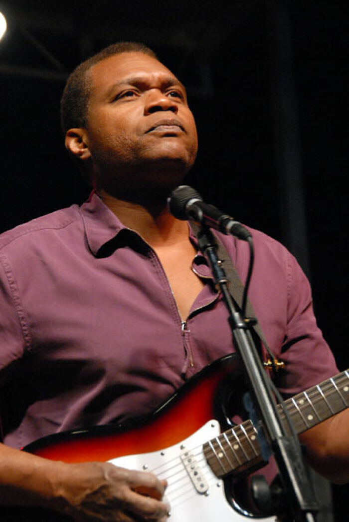 Robert Cray performing live, playing a red and white electric guitar with intense focus. Showcases his musical career.