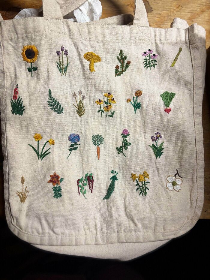 A canvas tote bag decorated with tiny, colorful hand-stitched floral embroidery projects