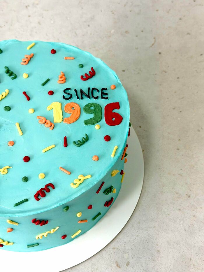 A light blue cake decorated with colorful sprinkles and the words Since 1996. Bakers prove treats look amazing and taste delicious.