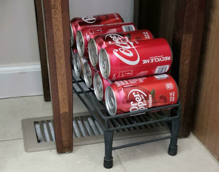 Clever solution: soda cans stacked neatly on a small shoe rack between furniture, random junk repurposed efficiently.