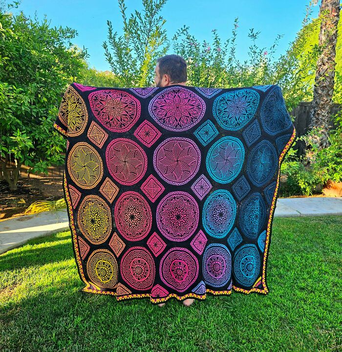 Bright crochet blanket with circular mandala designs held outdoors in sunlight