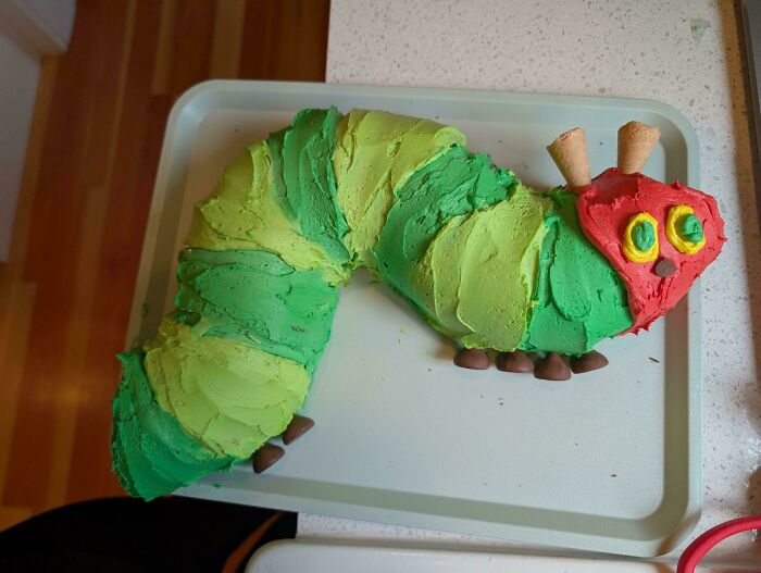 A green and red caterpillar-shaped cake on a white tray. Bakers prove treats look amazing and taste delicious.
