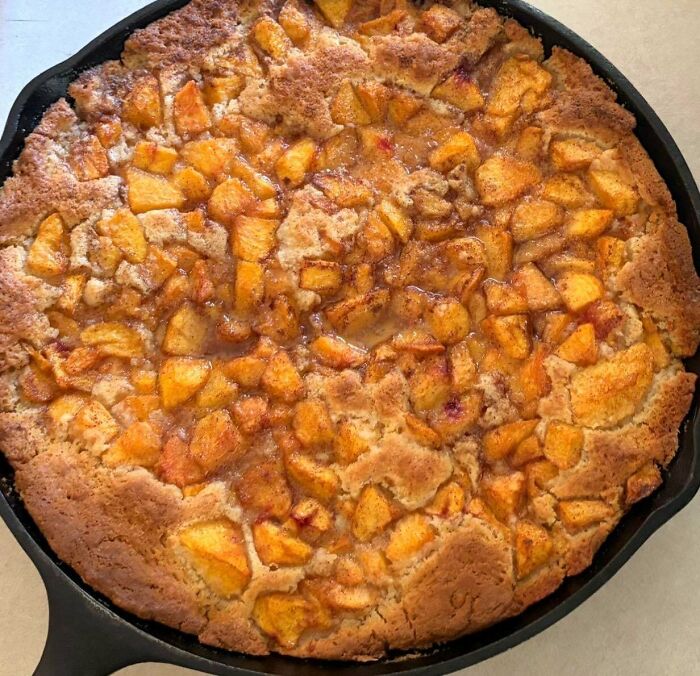 A cast iron skillet filled with a baked peach cobbler. Bakers prove treats look amazing and taste delicious.