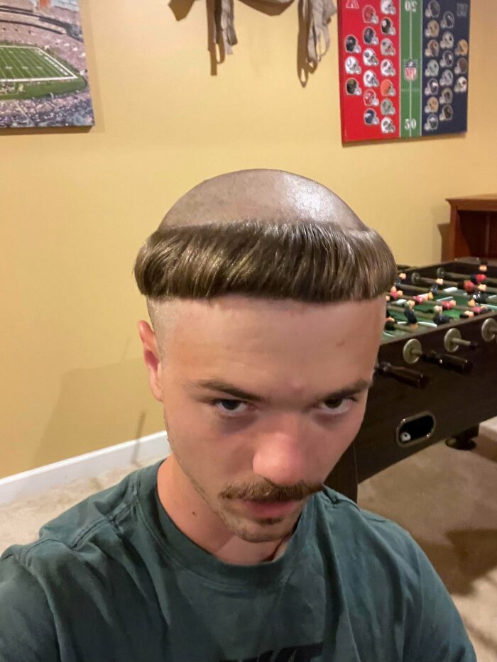 A young man with a bold monk-like bowl cut hairstyle, looking directly at the camera with a smirk.