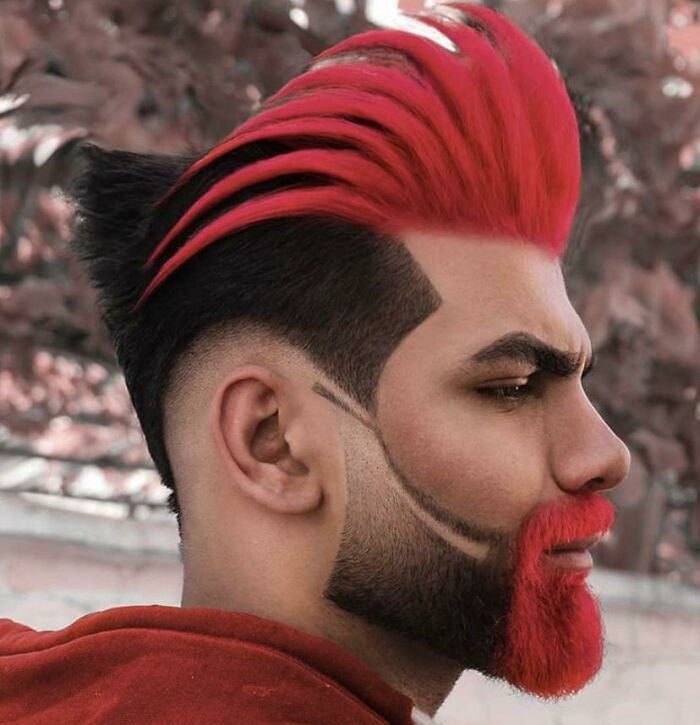 A man with a bold hairstyle, featuring vibrant red spiked hair and a matching red beard.