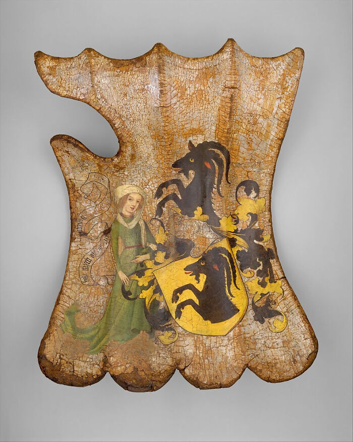 Painted wooden shield with a coat of arms and a woman in a green dress, from the Middle Ages.
